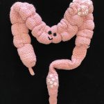 A crochet colon with eyes and smile.